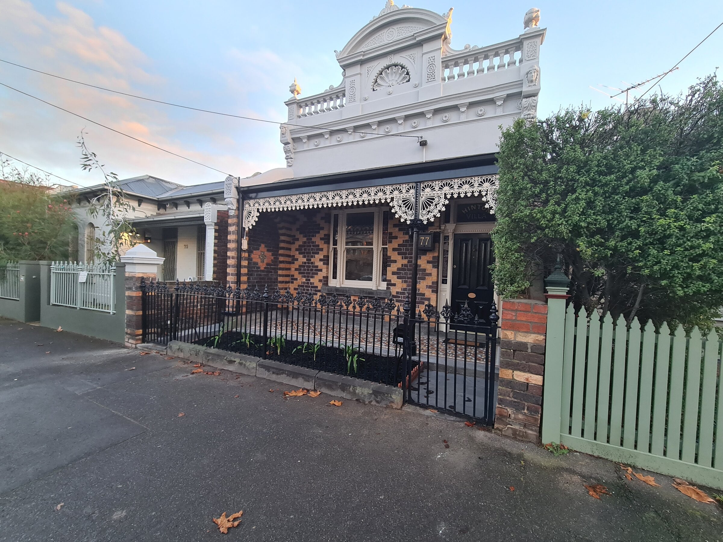 Victorian house front with patterned brickwork, cast-iron lace and a front garden