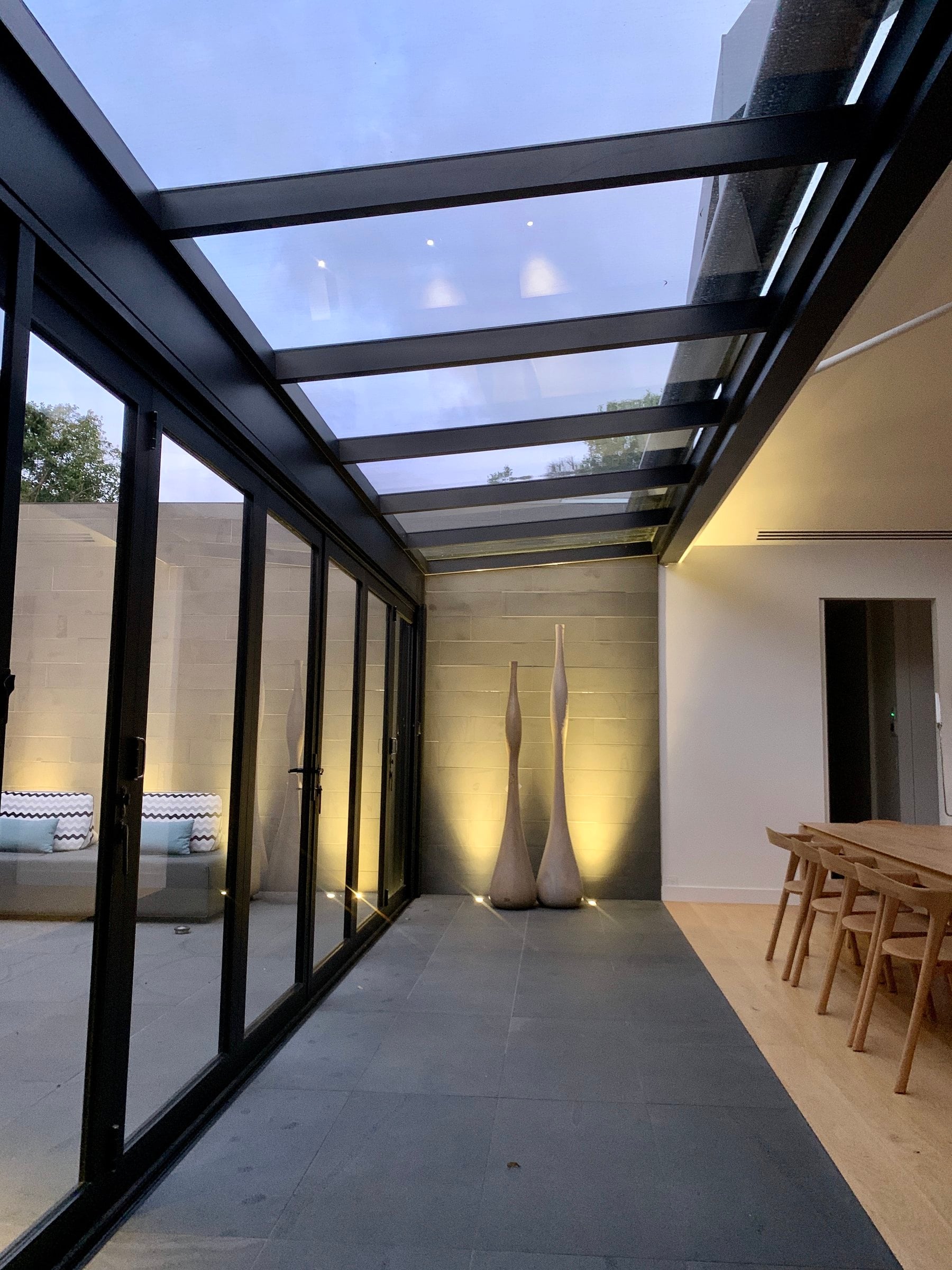 Walkway under a glass roof, dark stone paving and full-height glazing to the courtyard, Mount Martha