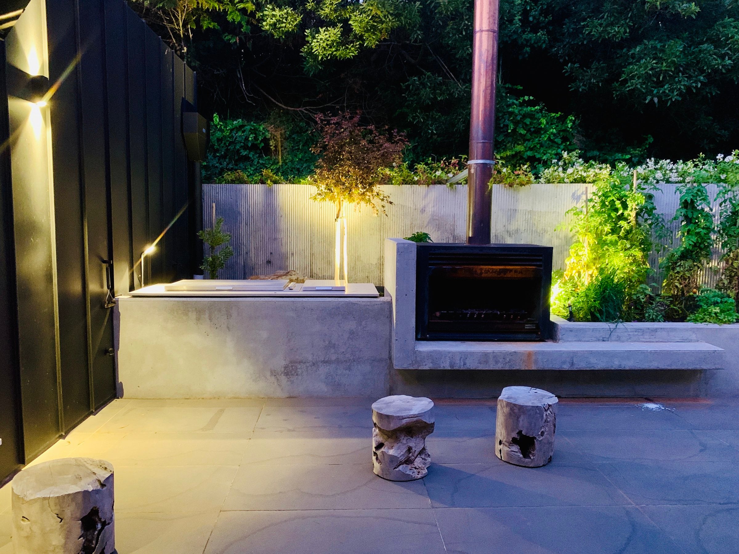 Courtyard at dusk with a concrete bench, an outdoor fireplace and timber stools, Mount Martha
